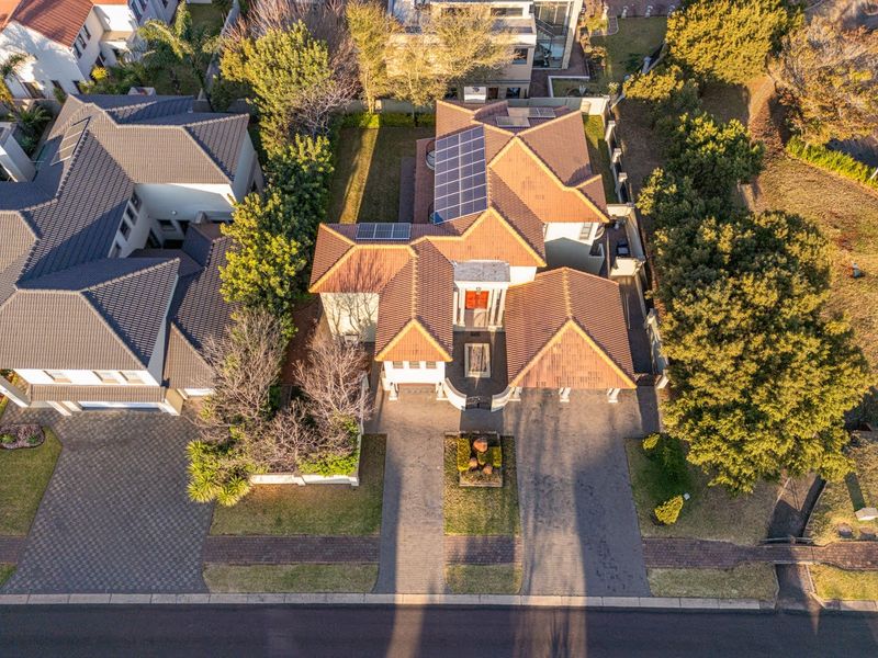 Aerial view of a residential property featuring a tiled roof with solar panels, a paved driveway, and established garden surroundings.