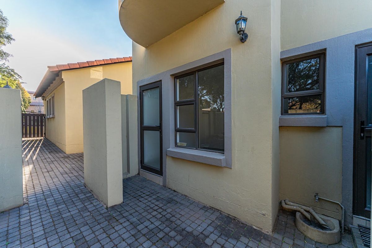 A paved rear courtyard area featuring aluminium window frames, an external wall light, and an outdoor water tap with exposed plumbing.