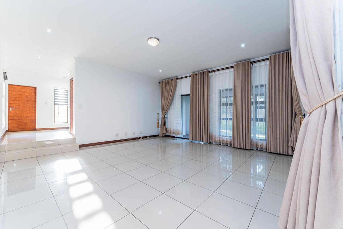 Spacious, light-filled living area featuring neutral tiled flooring, recessed lighting, and large sliding glass doors leading to the exterior.