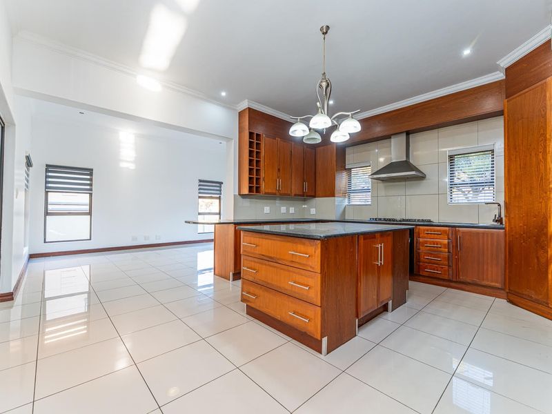 Spacious open-plan kitchen featuring warm wooden cabinetry, granite countertops, a central island, and sleek tiled flooring, seamlessly flowing into the adjacent living area.