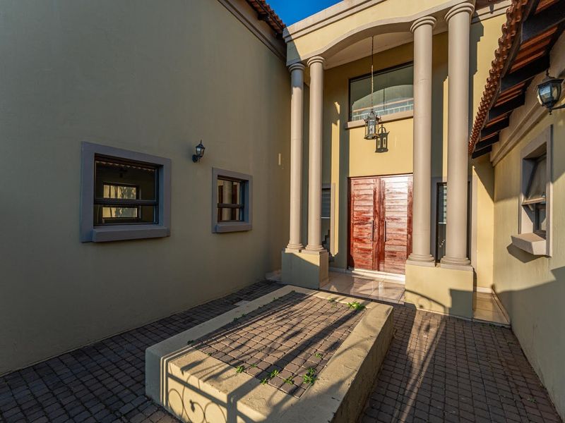 A grand entrance featuring a double wooden door, classical columns, and a paved courtyard with a built-in planter box.