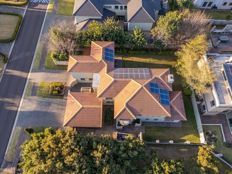 Aerial view of the property showcasing the tiled roof with integrated solar panels, surrounding landscaped garden, and paved driveway access.