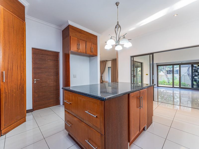 A spacious kitchen featuring a central island with granite countertops, wooden cabinetry, and tiled flooring, opening onto an outdoor area through sliding glass doors.