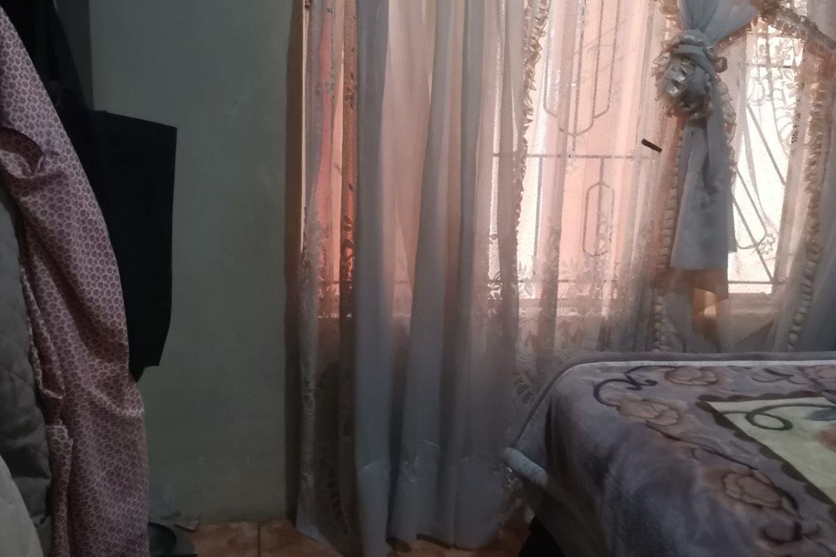 A bedroom interior featuring tiled flooring and a window with security gate protection.