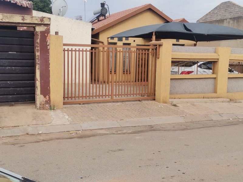 Front exterior view of the property featuring a metal sliding gate, perimeter wall, carport, and tiled roof structure.