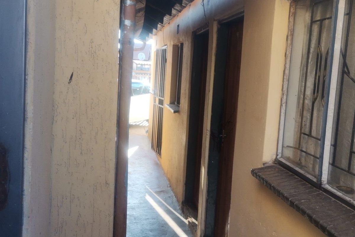 A narrow exterior side passage featuring concrete flooring, security bars on windows, and weathered exterior wall finishes.