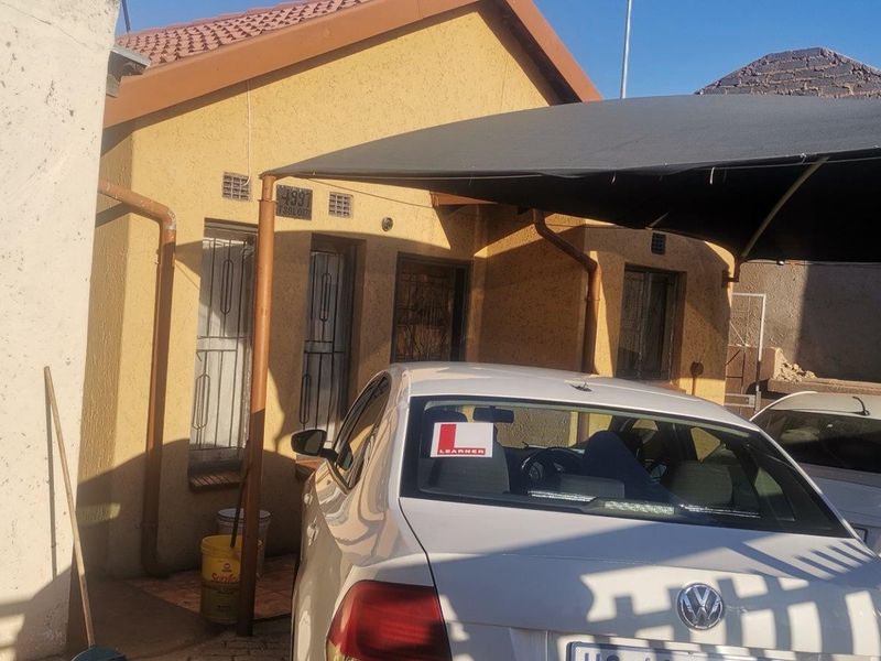 Front elevation of a residential house featuring a tiled roof, security gates, and a shade cloth carport structure.