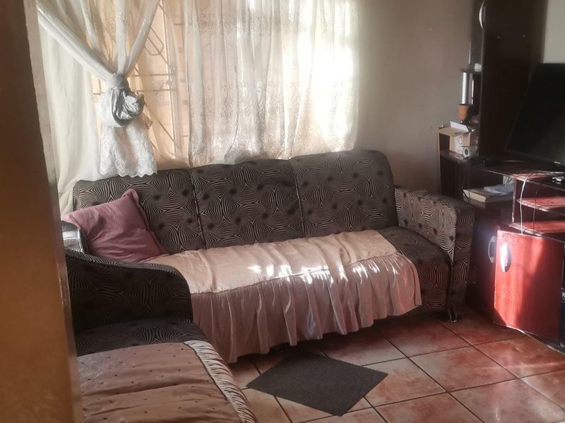 A compact living room area featuring tiled flooring and natural light filtered through window security bars.