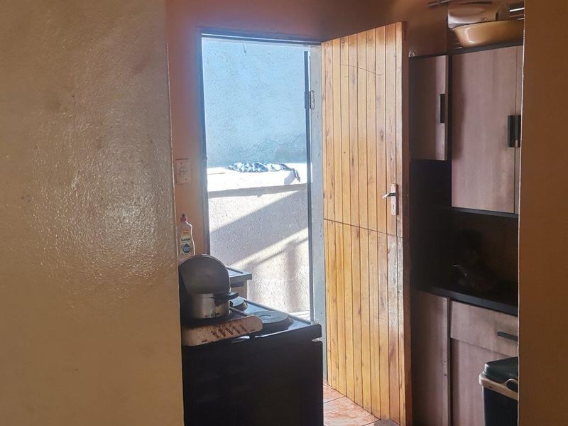 A compact kitchen area featuring built-in cabinetry and direct access to an outdoor space through a wooden door.
