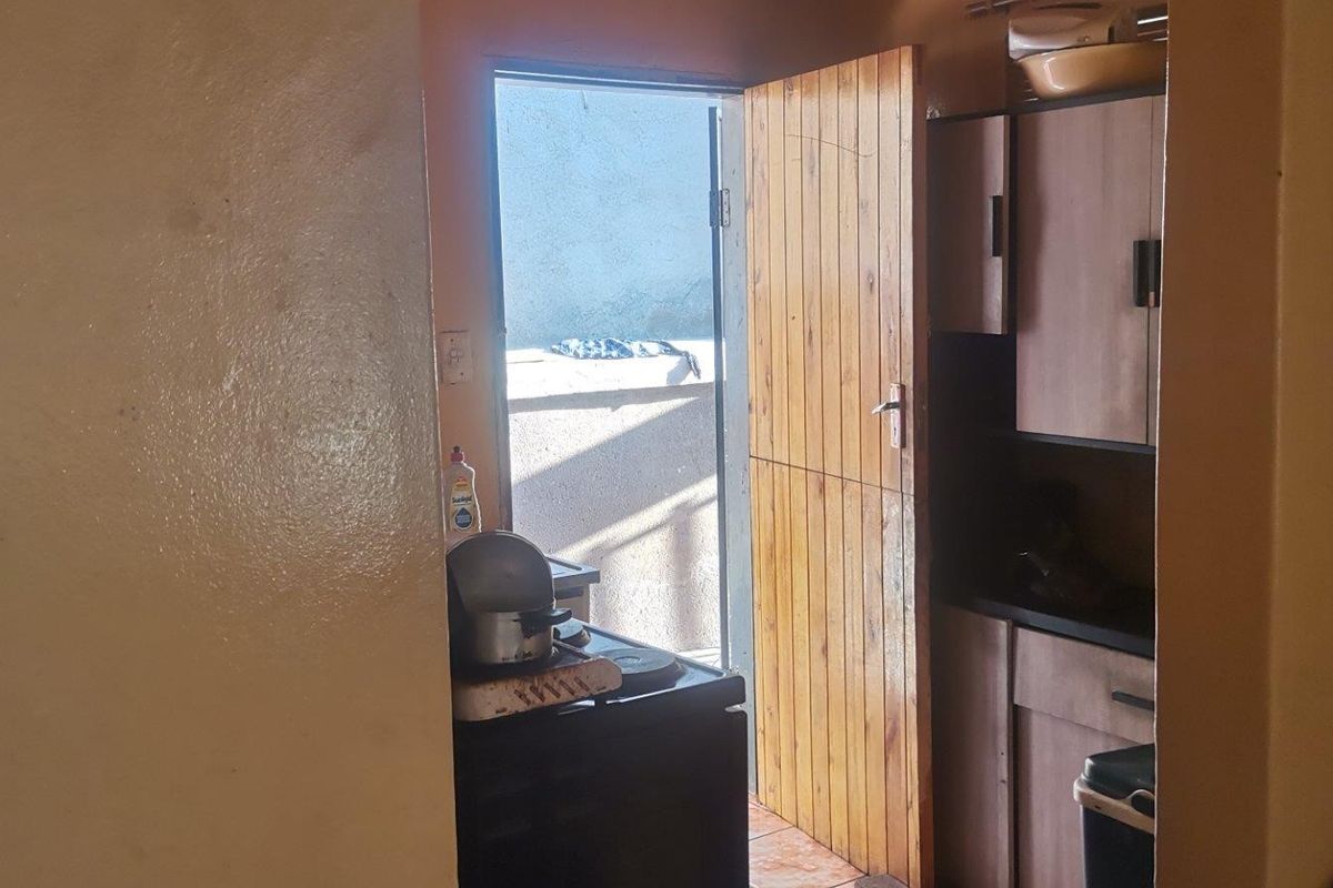 A compact kitchen area featuring built-in cabinetry and direct access to an outdoor space through a wooden door.