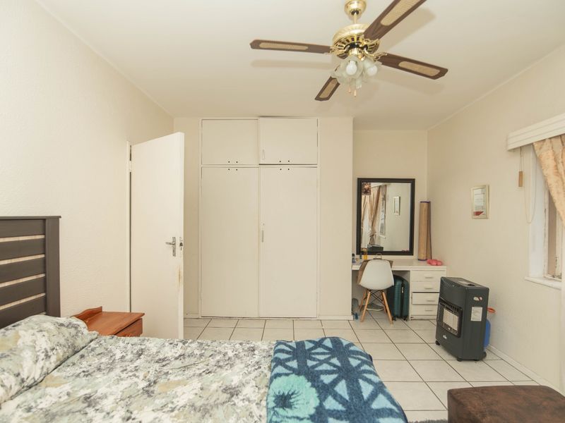 A bedroom featuring tiled flooring, built-in cupboards, and a ceiling fan, offering a functional space with potential for cosmetic updates.
