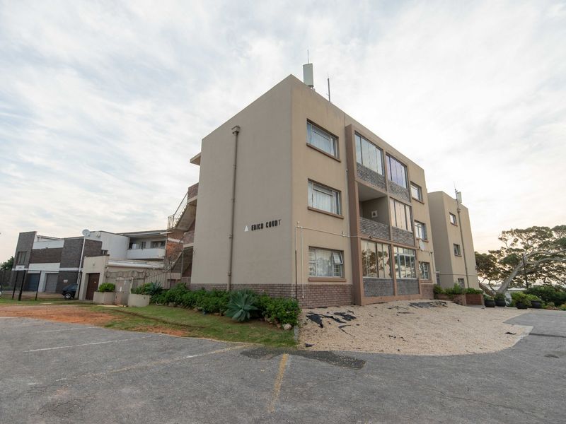 Exterior view of Erica Court apartment building featuring a multi-story facade, external staircases, and an adjacent asphalt parking area.