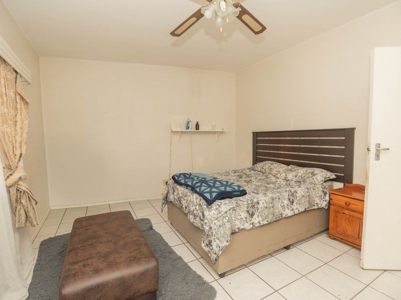 A functional bedroom featuring tiled flooring, a ceiling fan, and a wall-mounted shelf, offering a neutral base for personalization.