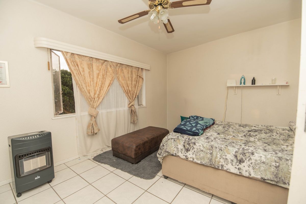 A bedroom featuring tiled flooring, a ceiling fan, and a wall-mounted shelf, offering a functional space ready for cosmetic updates.