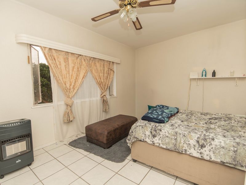 A bedroom featuring tiled flooring, a ceiling fan, and a wall-mounted shelf, offering a functional space ready for cosmetic updates.