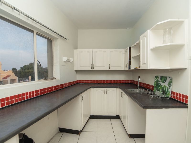 A functional kitchen featuring white built-in cabinetry, dark laminate countertops, a tiled backsplash, and a stainless steel sink with a view of the exterior.