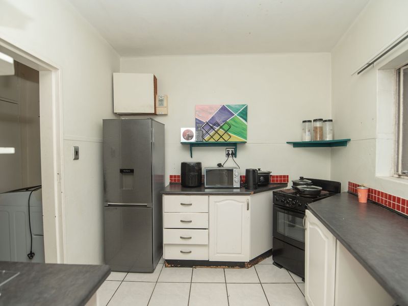 A functional kitchen featuring white cabinetry, dark laminate countertops, a tiled backsplash, and a freestanding stove, with an adjacent laundry area visible.