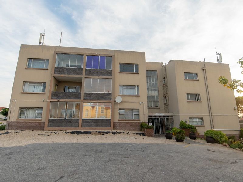 Front exterior view of a multi-story apartment building featuring enclosed balconies, a secure entrance, and an asphalt driveway area.