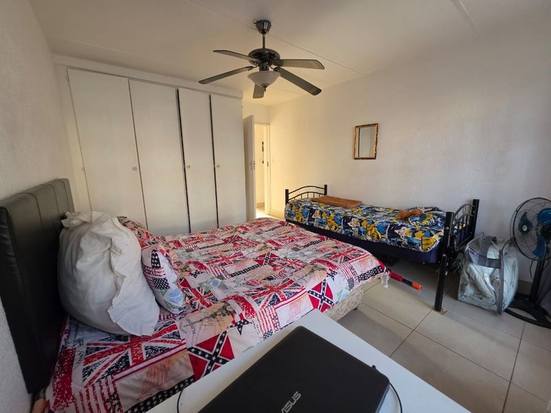 A bedroom featuring tiled flooring, a ceiling fan, and built-in cupboards providing ample storage space.