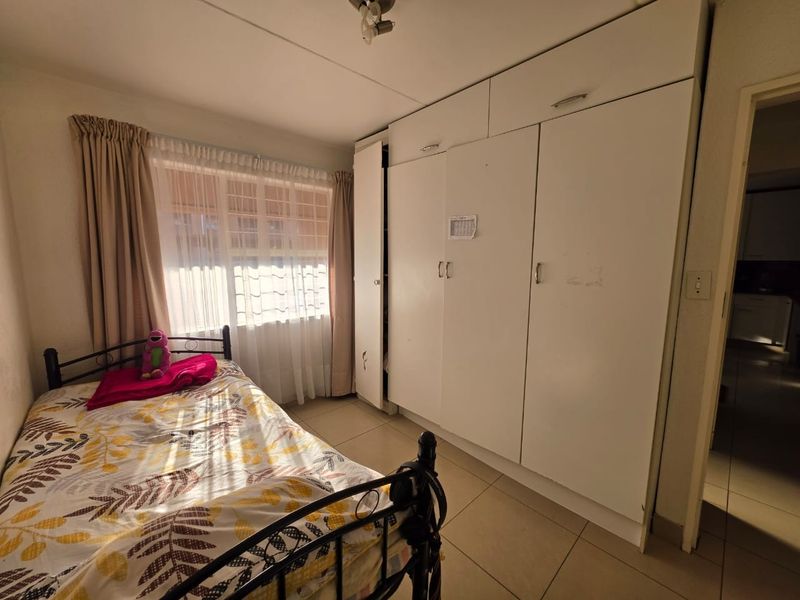 A functional bedroom featuring tiled flooring and extensive built-in cupboard storage, providing a practical layout for a standard apartment bedroom.