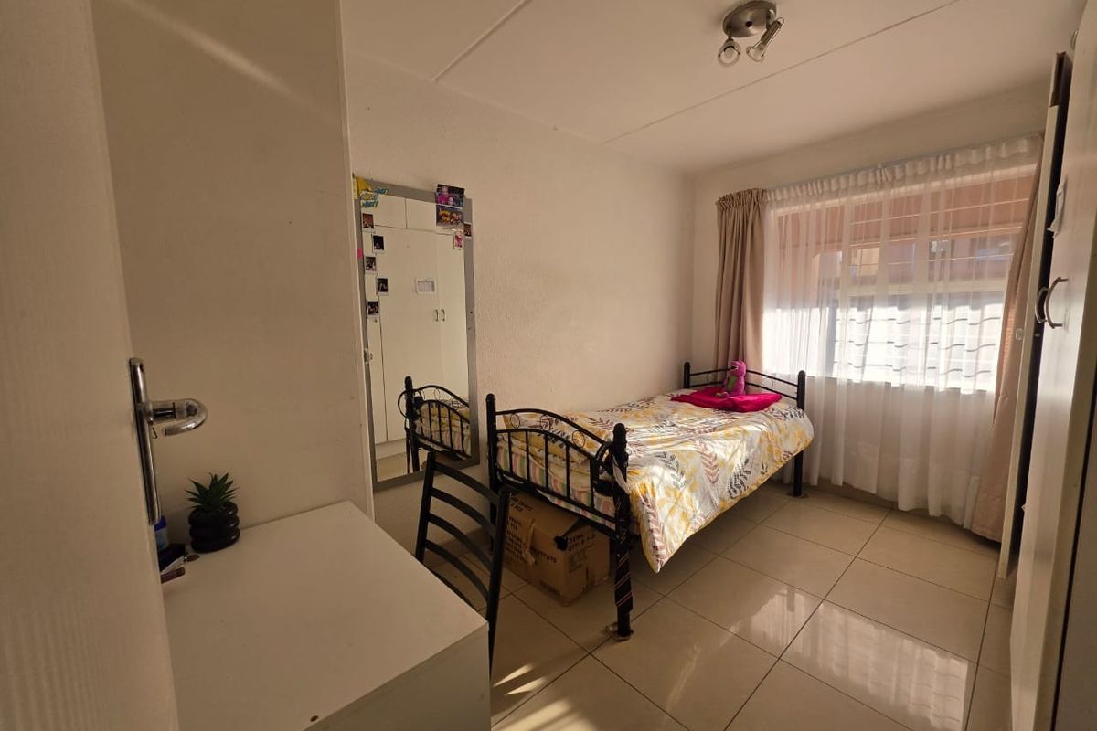 A functional bedroom featuring tiled flooring, a built-in wardrobe with a mirrored door, and natural light through a window with curtain tracks.