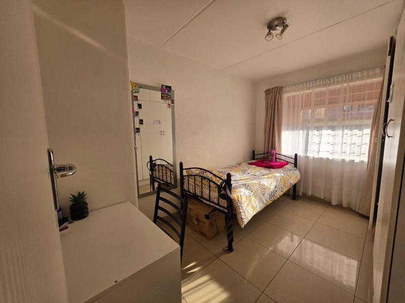 A functional bedroom featuring tiled flooring, a built-in wardrobe with a mirrored door, and natural light through a window with curtain tracks.