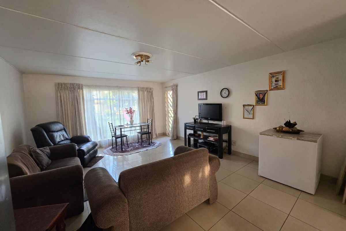 A spacious living room featuring neutral tiled flooring and large windows with curtain tracks, offering a bright and functional open-plan living area.