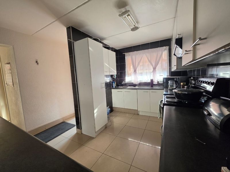 A functional kitchen featuring white cabinetry, black tiled backsplash, tiled flooring, and a built-in extractor fan with a freestanding stove.
