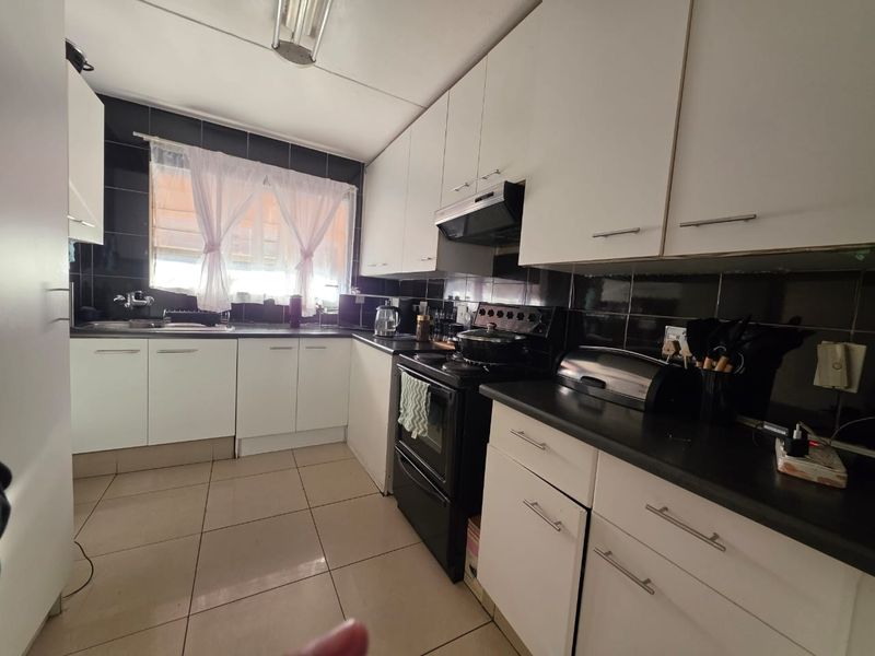 Functional kitchen featuring white cabinetry, black tiled backsplash, tiled flooring, and a built-in stove with extractor fan.