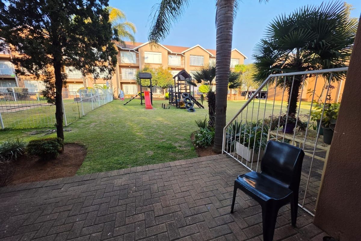 A view of a paved patio area overlooking a communal garden and playground within an apartment complex.