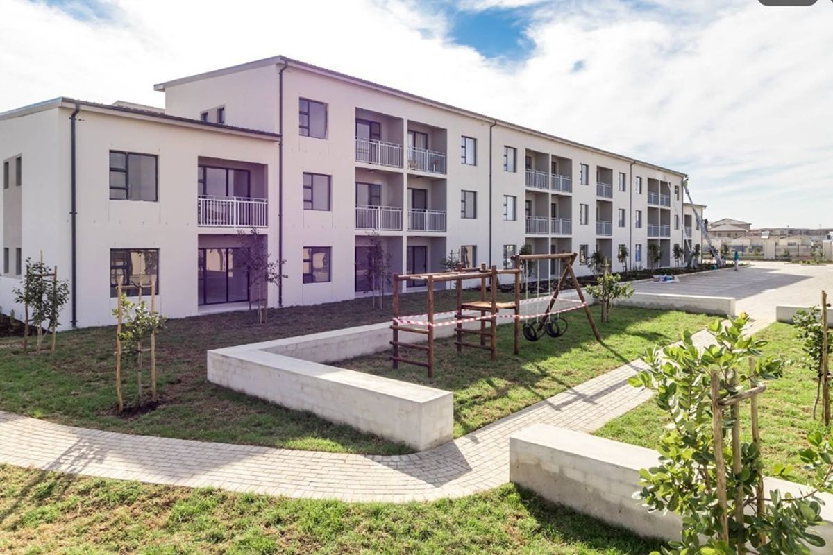 Exterior view of a modern apartment complex featuring private balconies, paved pathways, and a communal garden area with concrete landscaping elements.