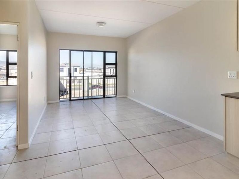An open-plan living area featuring neutral tiled flooring, clean walls, and a sliding glass door leading to a balcony, with an adjacent kitchen section.