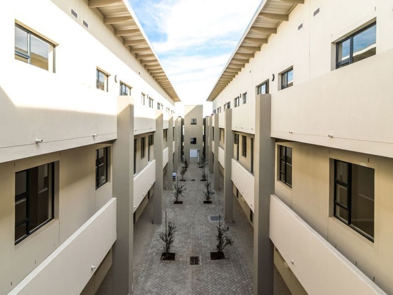 A symmetrical view of the apartment complex courtyard featuring paved walkways, structured landscaping, and multi-level exterior access corridors.
