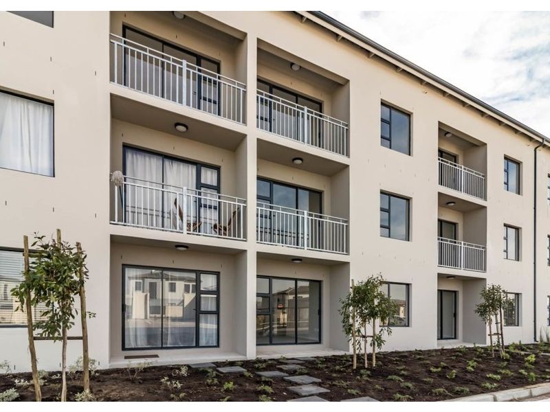 A modern apartment building exterior featuring multiple levels of balconies with metal railings and sliding glass doors, set above a landscaped garden area.
