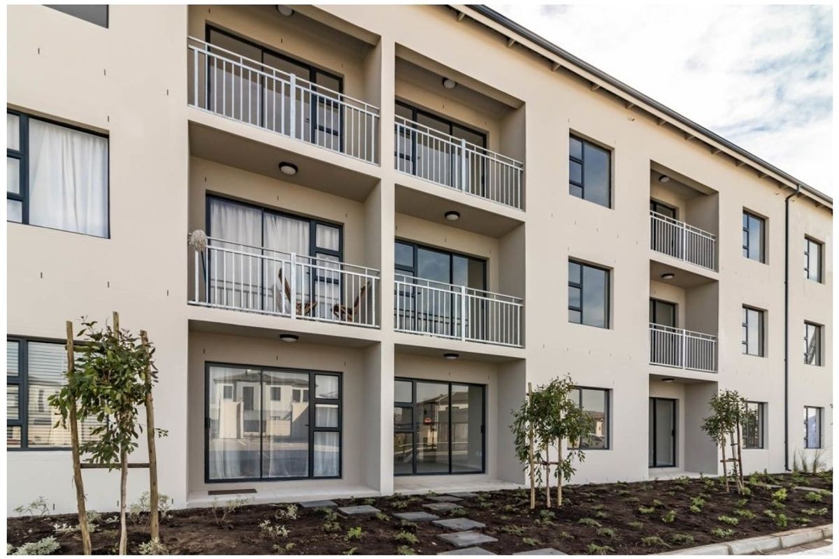 A modern apartment building exterior featuring multiple levels of balconies with metal railings and sliding glass doors, set above a landscaped garden area.