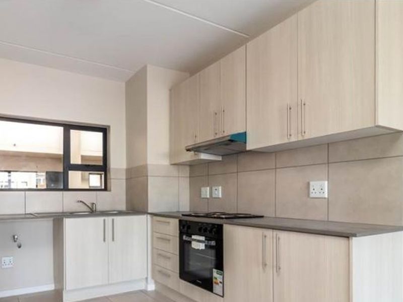 A clean, modern kitchen featuring light wood-tone cabinetry, integrated oven and hob, tiled backsplash, and ample counter space in an open-plan layout.