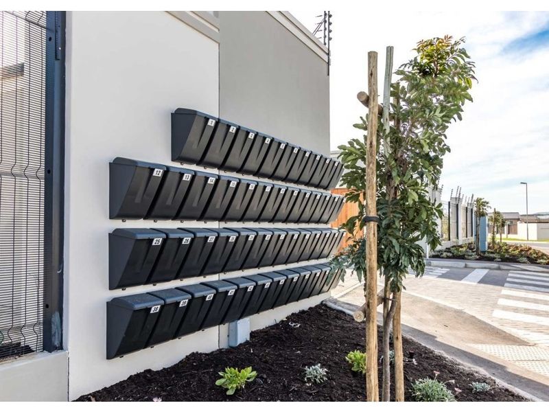 Exterior view of the apartment complex entrance featuring a modern bank of numbered mailboxes and secure perimeter fencing.
