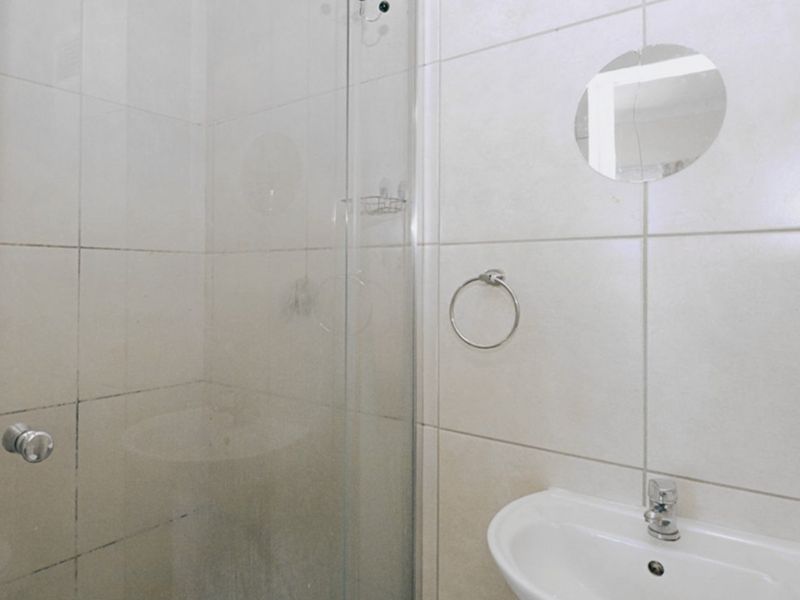 A functional bathroom featuring a glass shower enclosure, wall-mounted basin with chrome mixer tap, and neutral ceramic wall tiling.