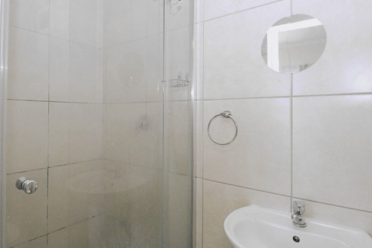 A functional bathroom featuring a glass shower enclosure, wall-mounted basin with chrome mixer tap, and neutral ceramic wall tiling.