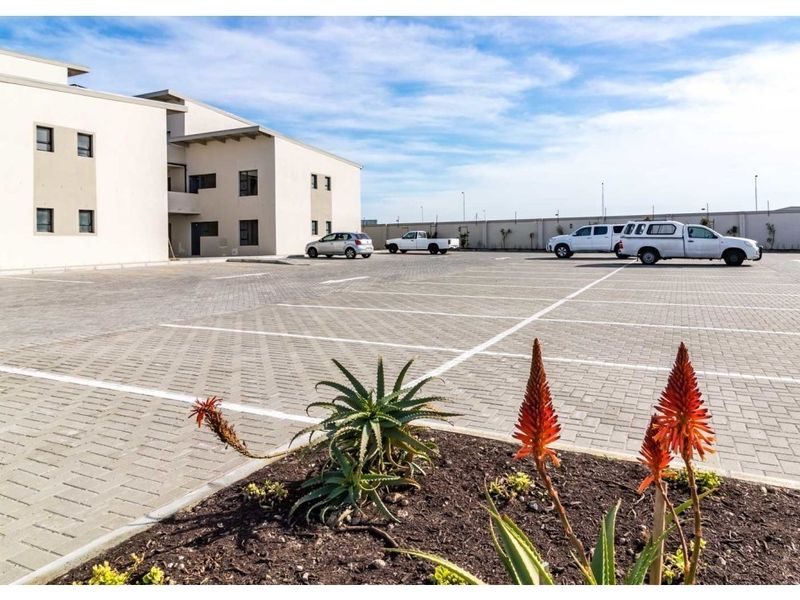 A view of the apartment complex exterior featuring a paved parking area and landscaped garden beds.