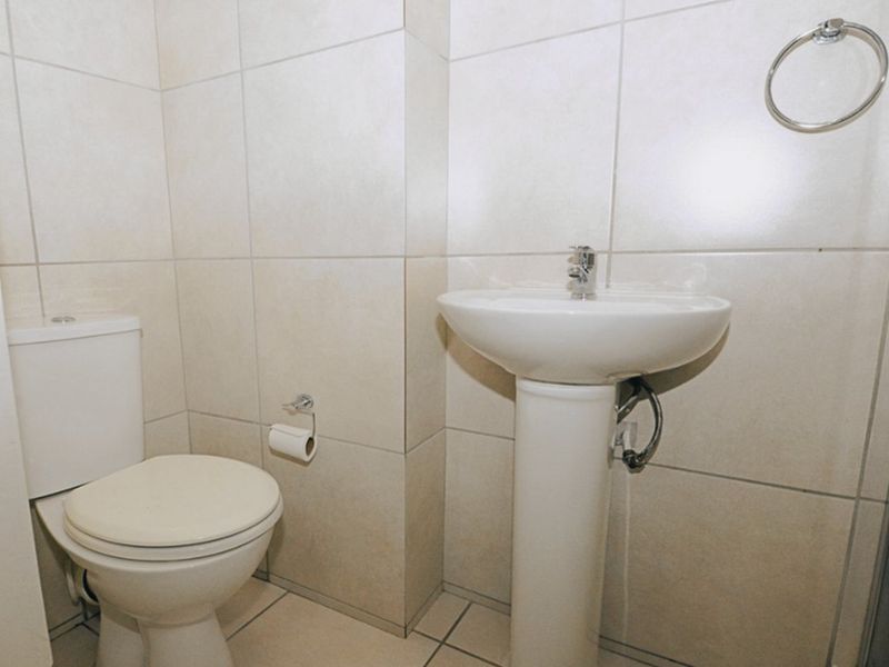 A clean, functional bathroom featuring a pedestal basin, toilet, and neutral floor-to-ceiling wall tiling.