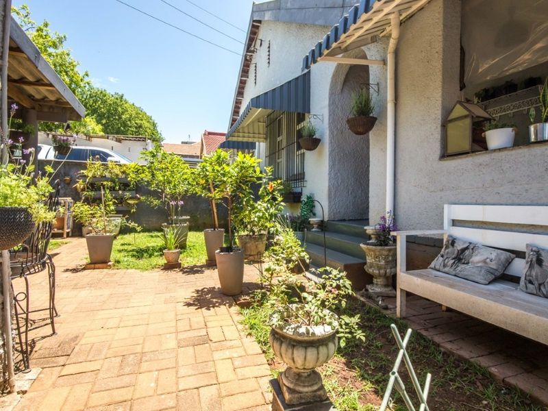 A charming front entrance area featuring brick paving, a covered porch with an awning, and a well-maintained garden space.
