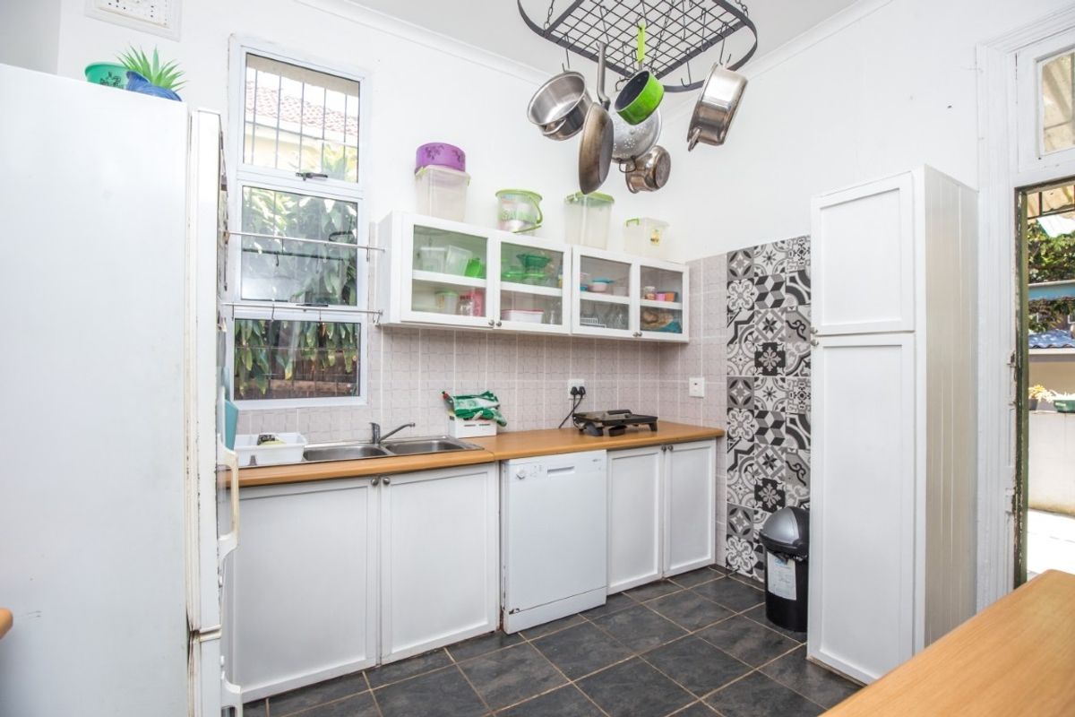 A functional kitchen featuring white cabinetry, laminate countertops, a double basin sink, and decorative tiled accents, providing ample storage and workspace.