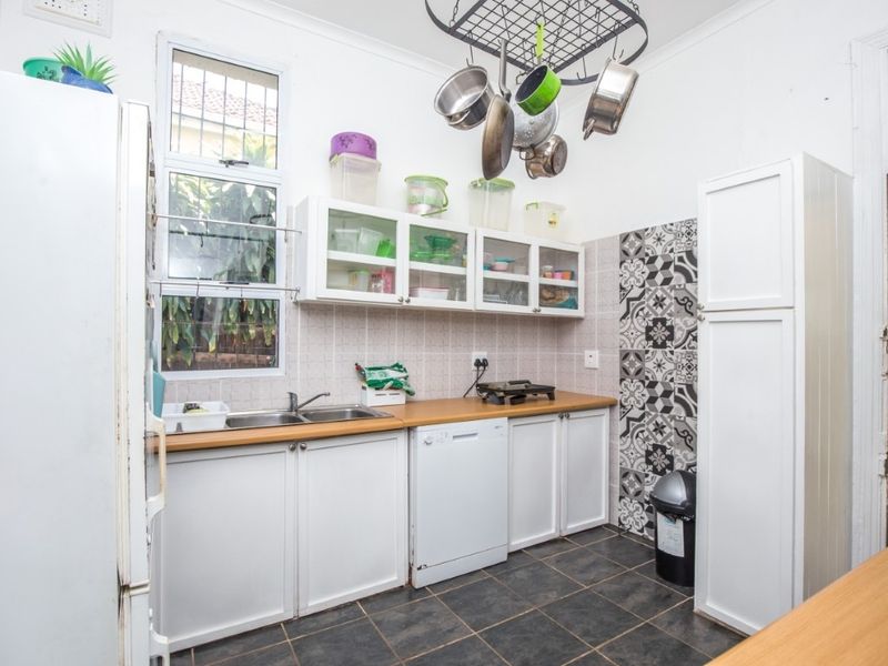 A functional kitchen featuring white cabinetry, laminate countertops, a double basin sink, and decorative tiled accents, providing ample storage and workspace.