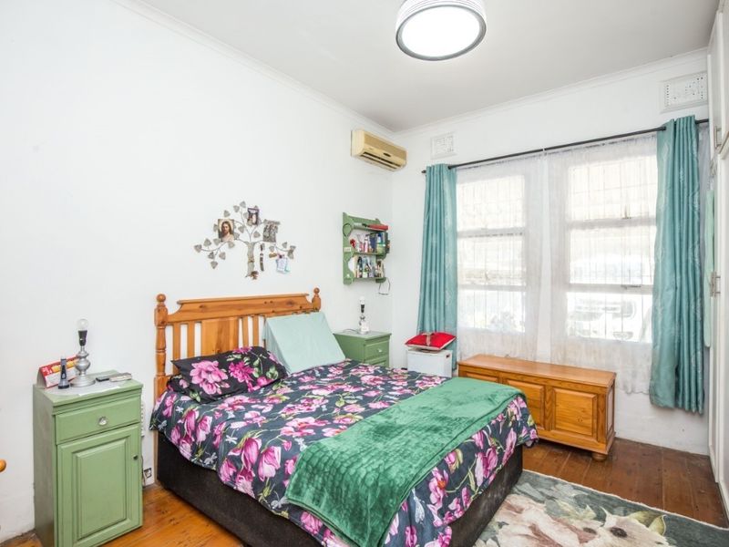 A well-lit bedroom featuring timber flooring, built-in cupboards, and a wall-mounted air conditioning unit.