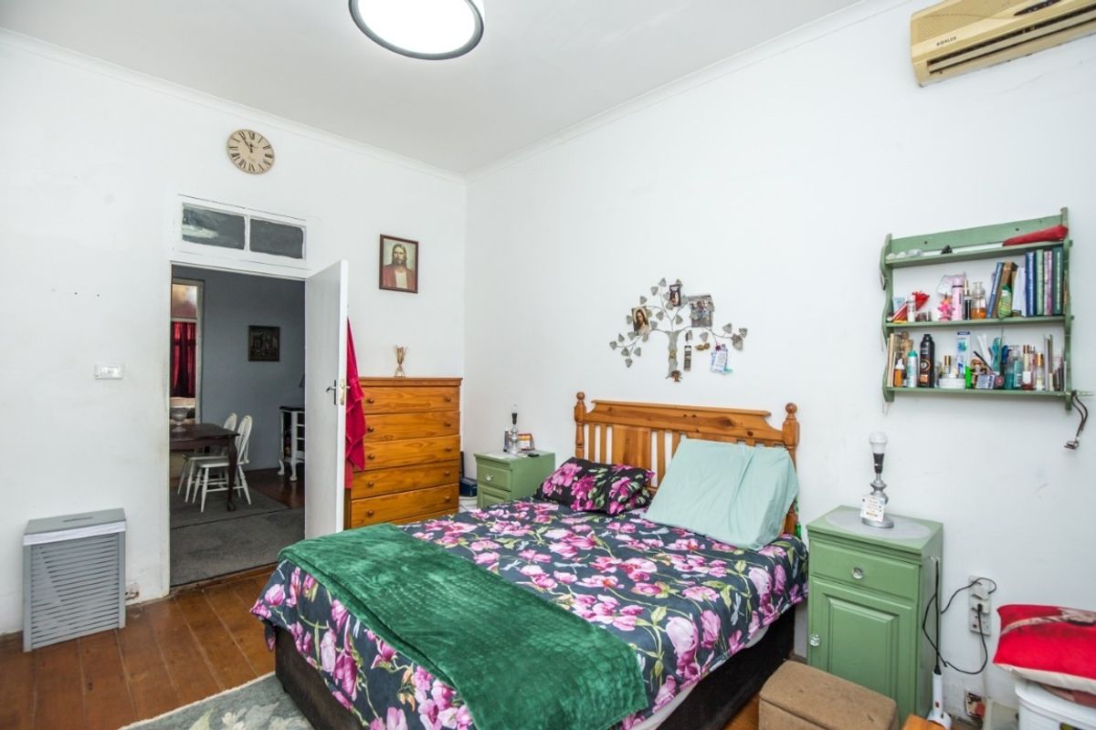 A bedroom featuring timber flooring, a wall-mounted air conditioning unit, and a transom window above the doorway.