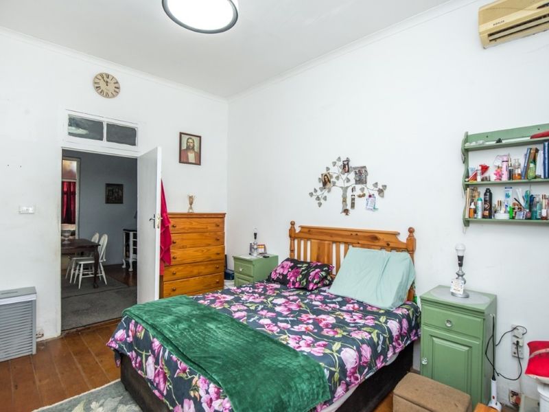 A bedroom featuring timber flooring, a wall-mounted air conditioning unit, and a transom window above the doorway.