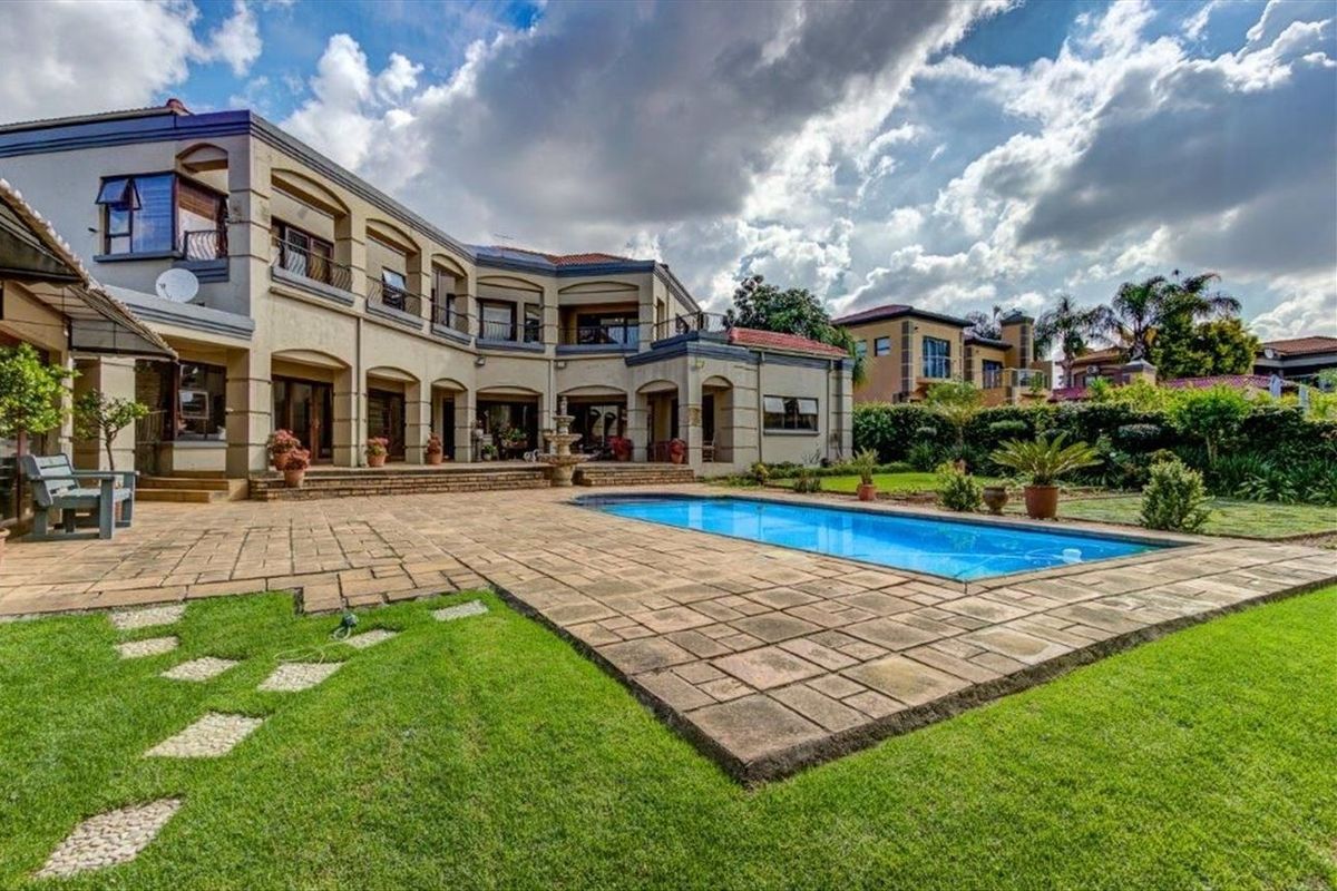 Spacious rear exterior featuring a large paved patio, swimming pool, landscaped garden, and a multi-level residence with balconies.