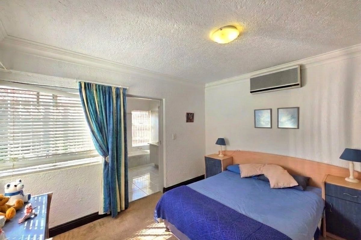 A functional bedroom featuring carpeted flooring, a wall-mounted air conditioning unit, and direct access to an adjoining en-suite bathroom.