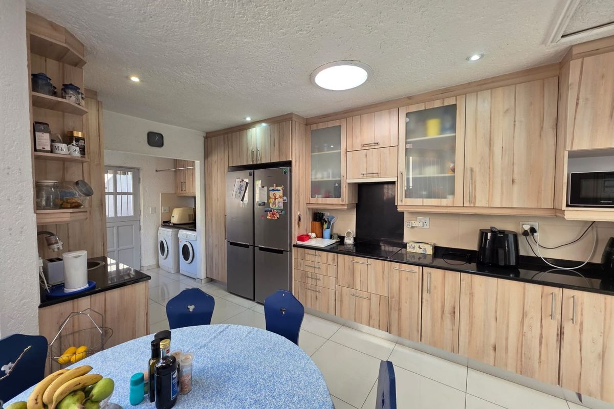 Functional kitchen featuring light wood-finish cabinetry, dark granite countertops, integrated microwave, and tiled flooring, with an adjacent laundry area.